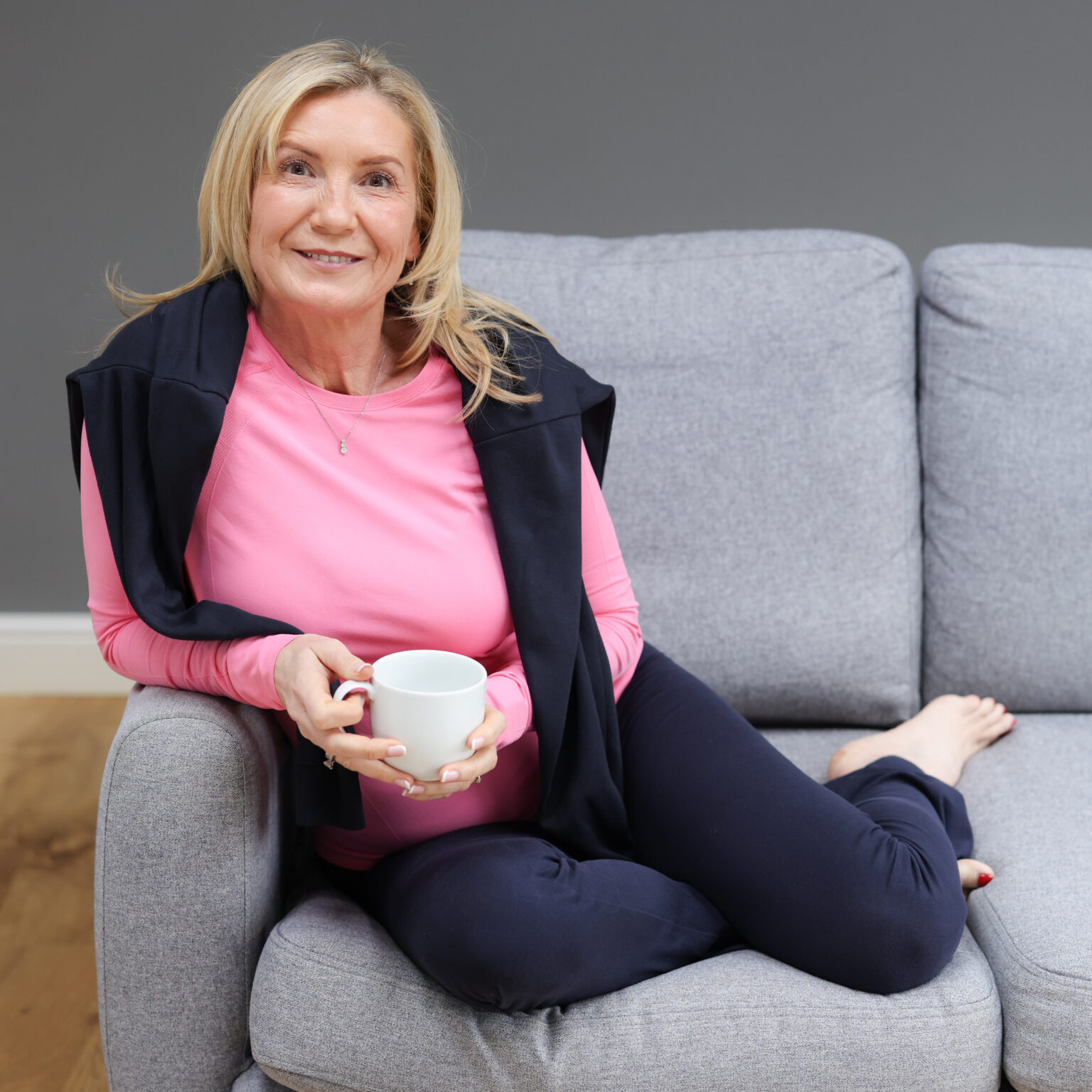 Julie Grimes seated on a grey sofa holding a white mug
