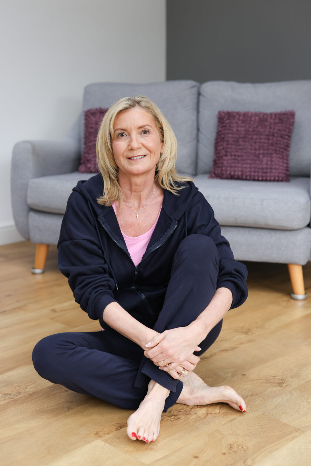 Julie Grimes sitting barefoot on a wooden floor in front of a grey sofa