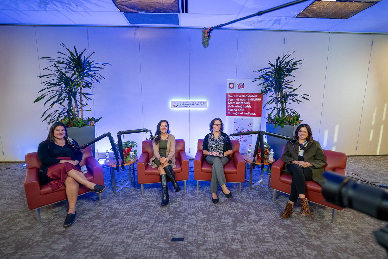 Maria Vought and three fellow panelists seated in red armchairs with podcast microphones on the NALHE Indiana Chapter Café con Leche panel stage
